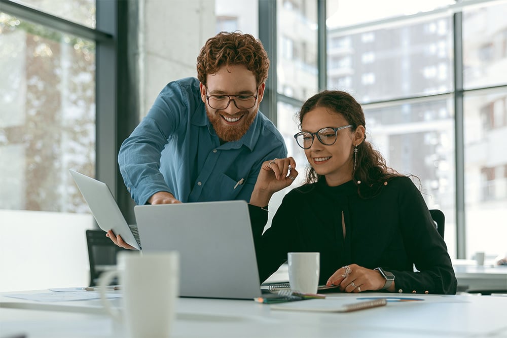 Zwei Menschen schauen gemeinsam auf einen Laptop in einem hellen Büro.